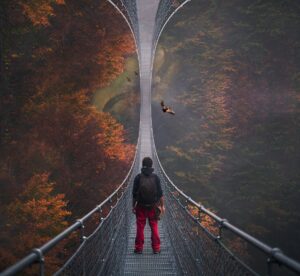Pessoa caminhando sobre uma ponte suspensa em meio à névoa e florestas outonais, simbolizando a jornada interior de Zadig e o processo de individuação na Leitura Terapêutica.